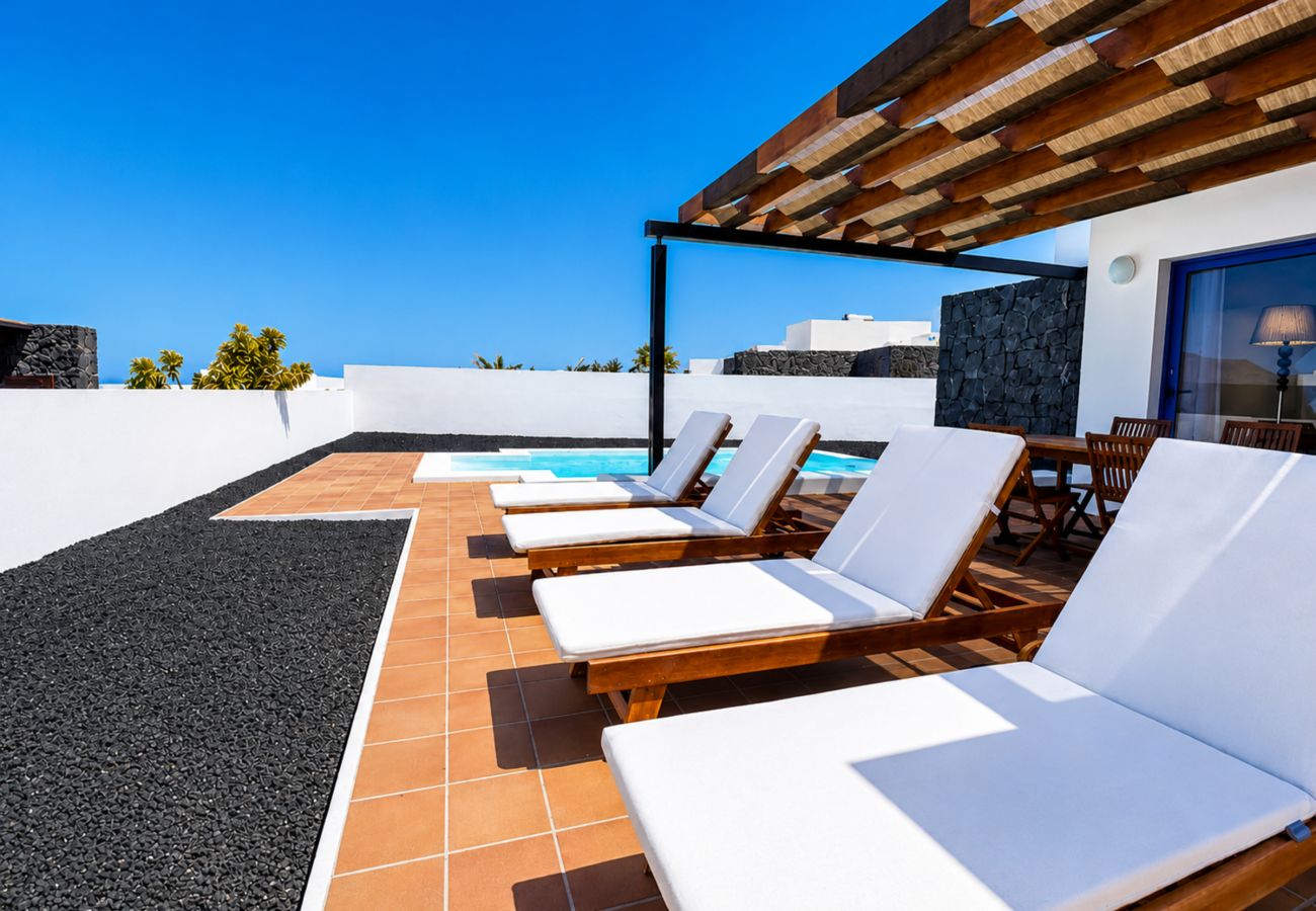 White loungers on terracotta floor under wooden pergola by the pool