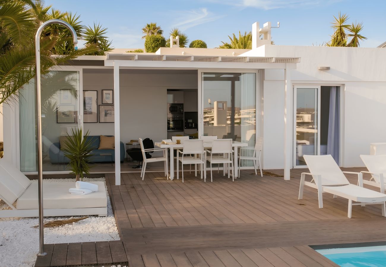 Outdoor terrace with wooden decking, shower, white loungers and table under pergola